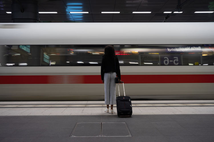 Rear view of woman with suitcase by train at railroad station platform