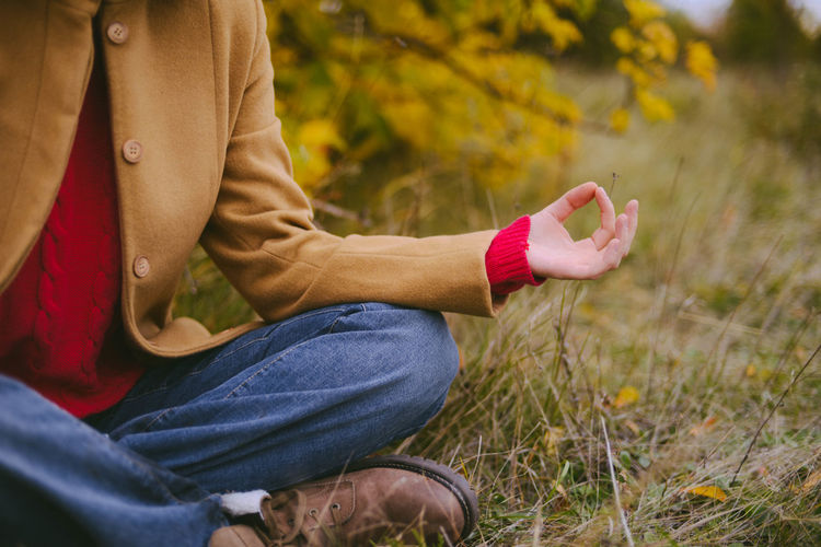 Low section of woman meditating on grassy field
