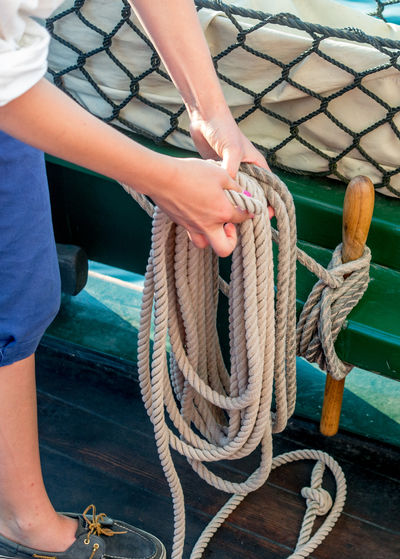 A sailor secures thick rope with a neat sailors knot, along the side of this tall ship 