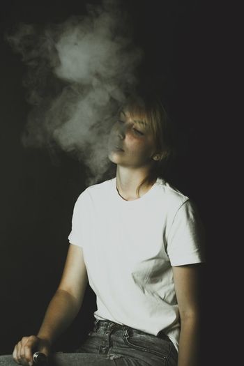 Woman exhaling smoke against black background