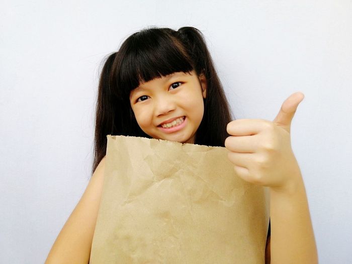 Portrait of smiling girl showing thumbs up against white background