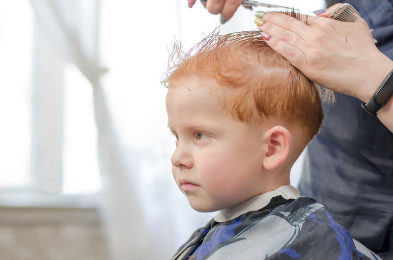 Child in a hairdressing salon. the hands of a hairdresser are cutting a 4-year-old boy