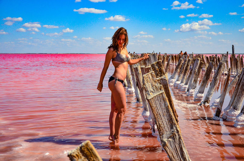 Full length of young woman standing in sea against sky