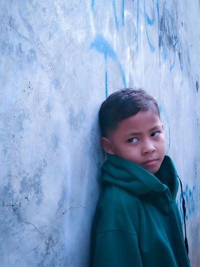 Portrait of young boy standing against wall