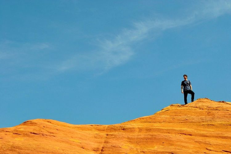 Low angle view of young man standing on cliff against blue sky