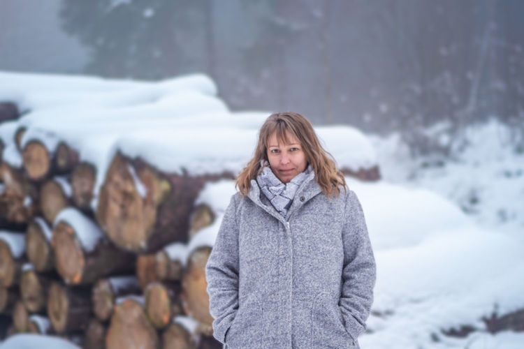 Portrait of woman standing against logs in snow