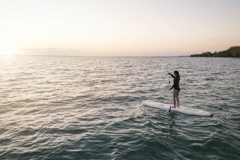 Woman paddleboarding on sea against sky during sunset