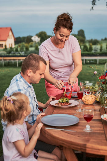 Family having a meal from grill during summer picnic outdoor dinner in a home garden