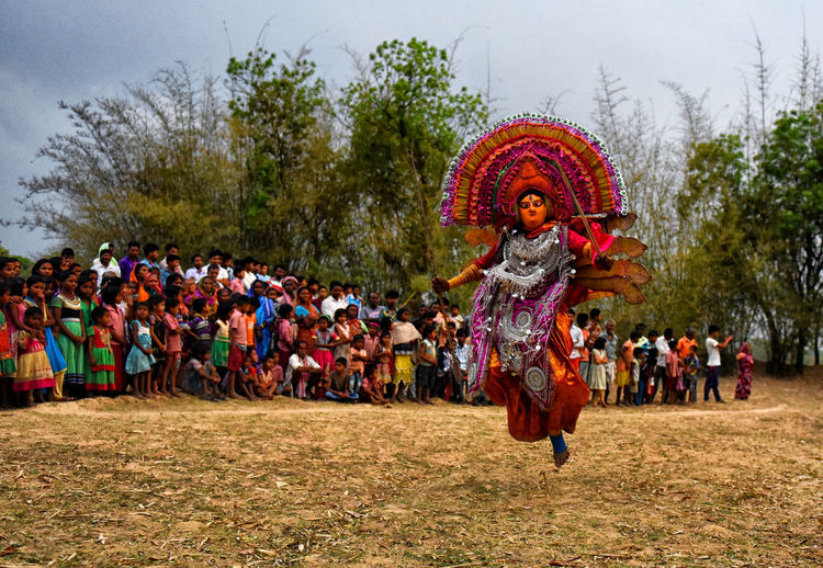 Crowd looking at chhau dance on field against sky