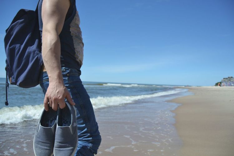 Midsection of man with shoes standing at beach