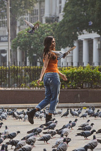 Full length of woman walking by birds on road