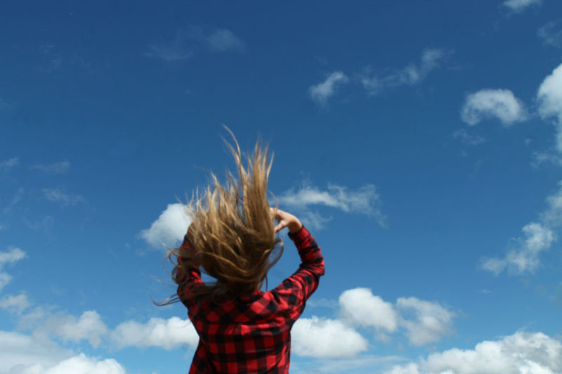 Low angle view of woman tossing hair against sky