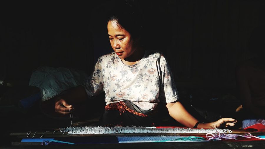 Mature woman weaving fabric while sitting at home