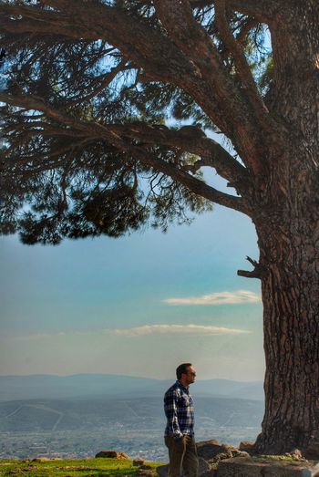 Man standing by tree trunk against sky