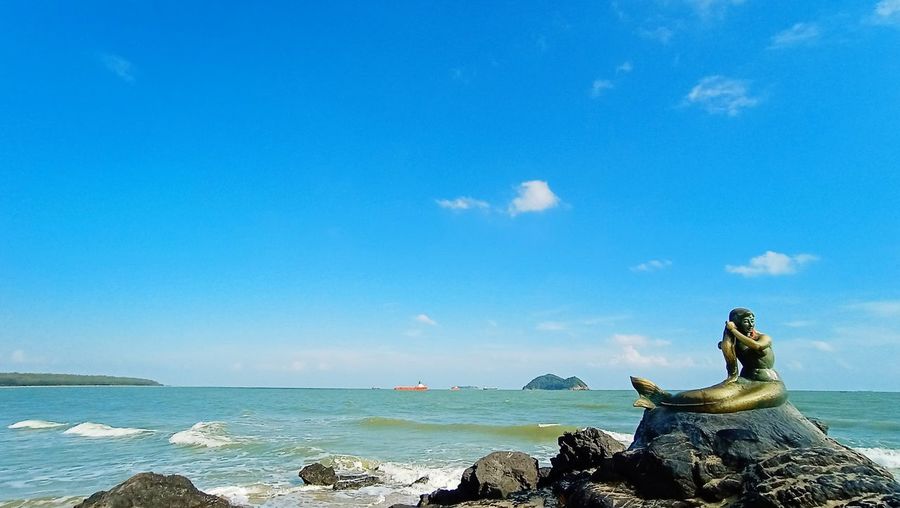 Statue by sea against blue sky
