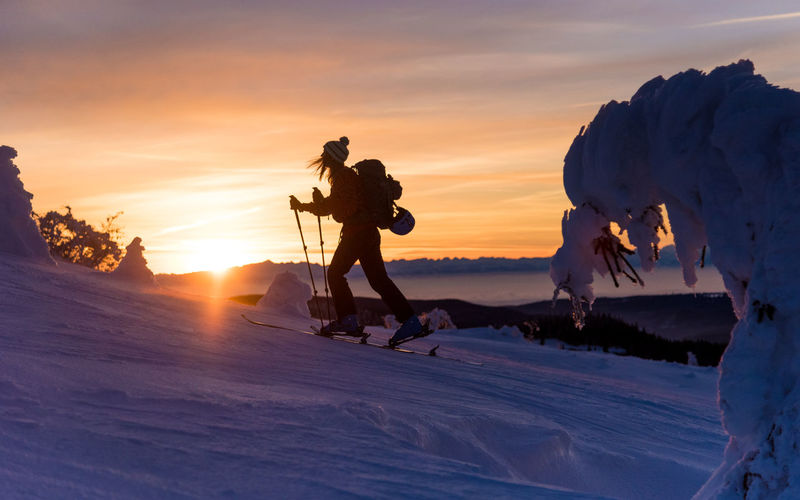 Silhouette woman skiing on snowcapped mountain during sunset