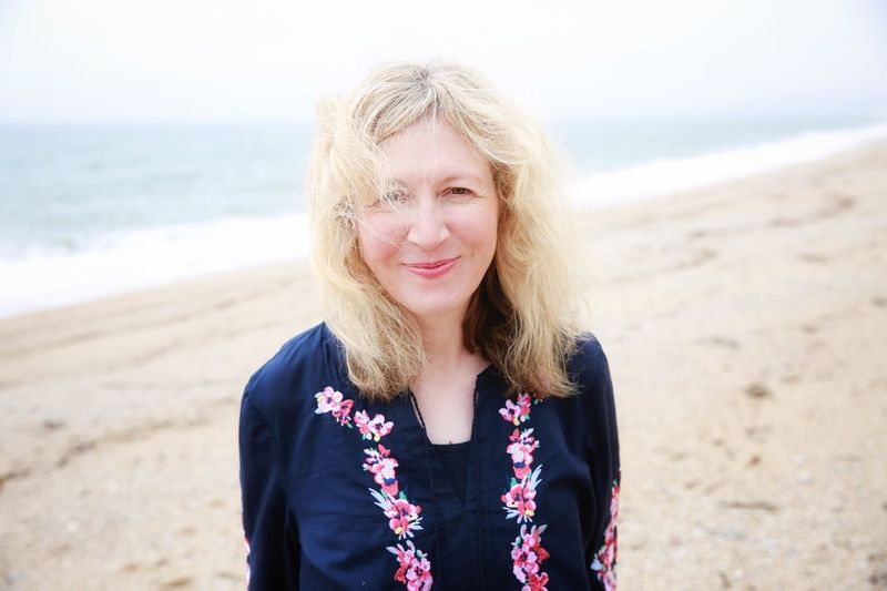 Portrait of smiling mature woman standing at beach against sky