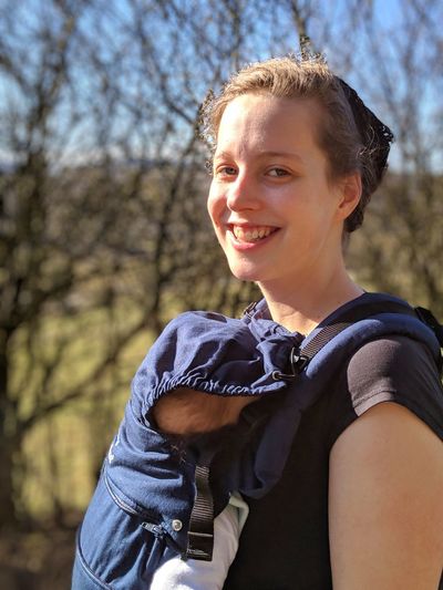 Portrait of smiling woman carrying baby against trees