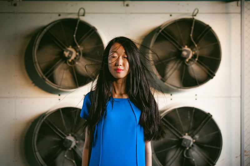 Young woman with tousled hair standing against exhaust fans
