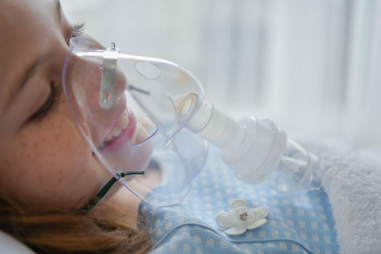 Close-up of girl wearing oxygen mask in hospital ward