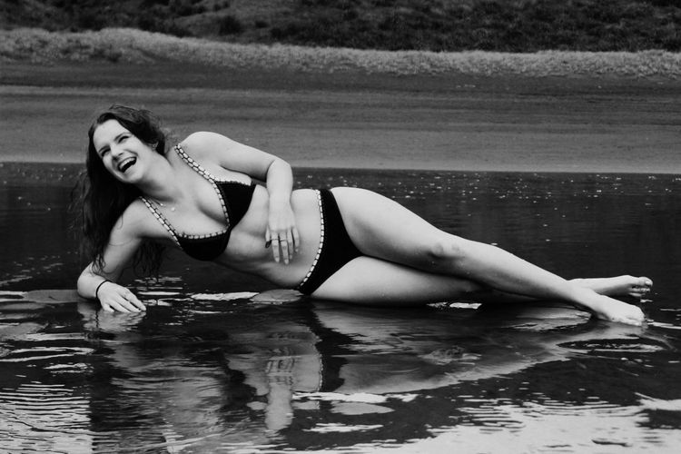 Happy teenage girl in bikini lying on shore at beach