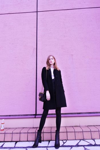 Full length portrait of woman standing against pink wall