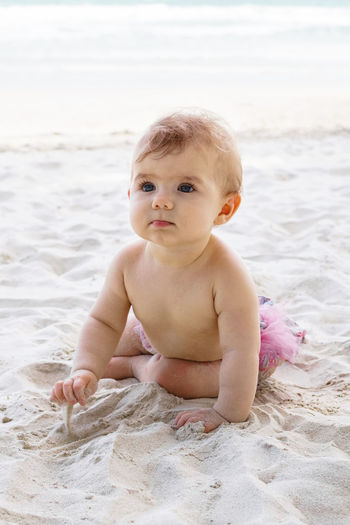 Candid portrait of adorable little baby girl on sand at beach on background of sea. 