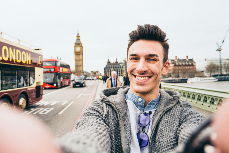 Portrait of smiling man standing on road against sky in city