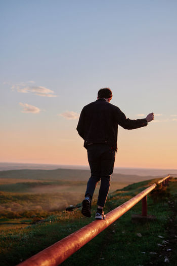 Rear view of man standing on beach against sky during sunset