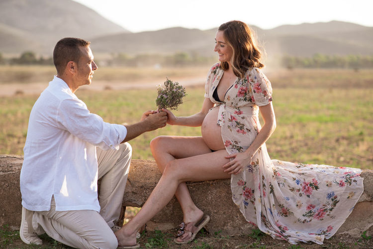 Man giving flowers to pregnant woman sitting on concrete