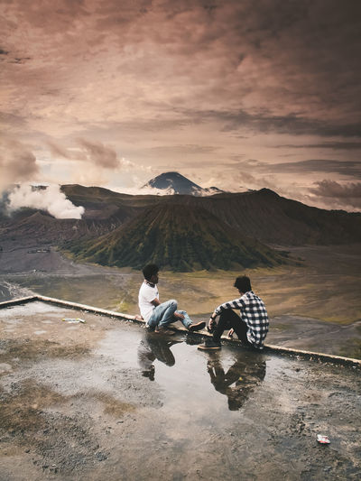 Men looking at mountains against cloudy sky