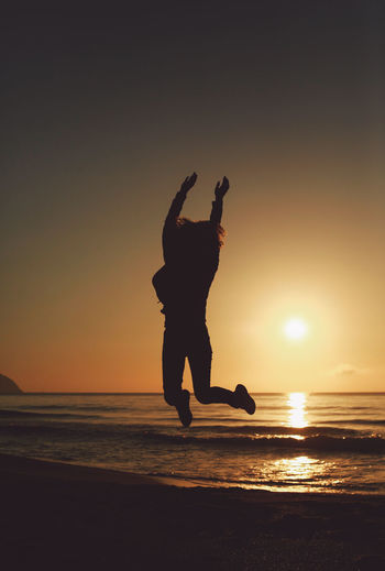 Silhouette woman jumping at beach against sky during sunset