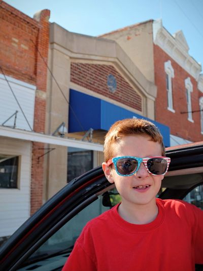 Portrait of boy wearing sunglasses while standing by car in city