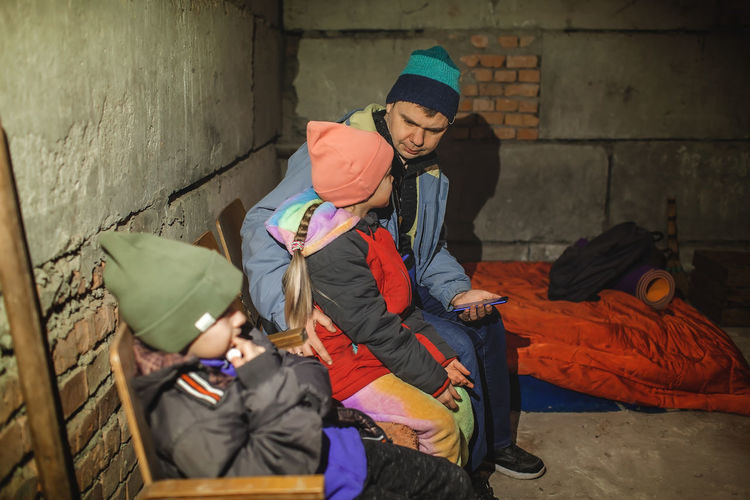 Ukrainian father with kids sits in bomb shelter and reads latest braking news about russian invaders