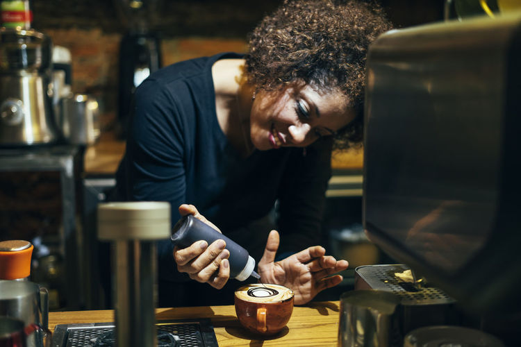 Male waitress barista working in coffee shop. prepare decorated coffee