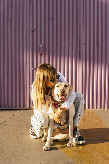 Woman kissing pet dog crouching in front of corrugated wall