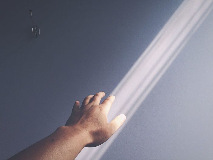 Cropped image of person touching sunlight falling on wall