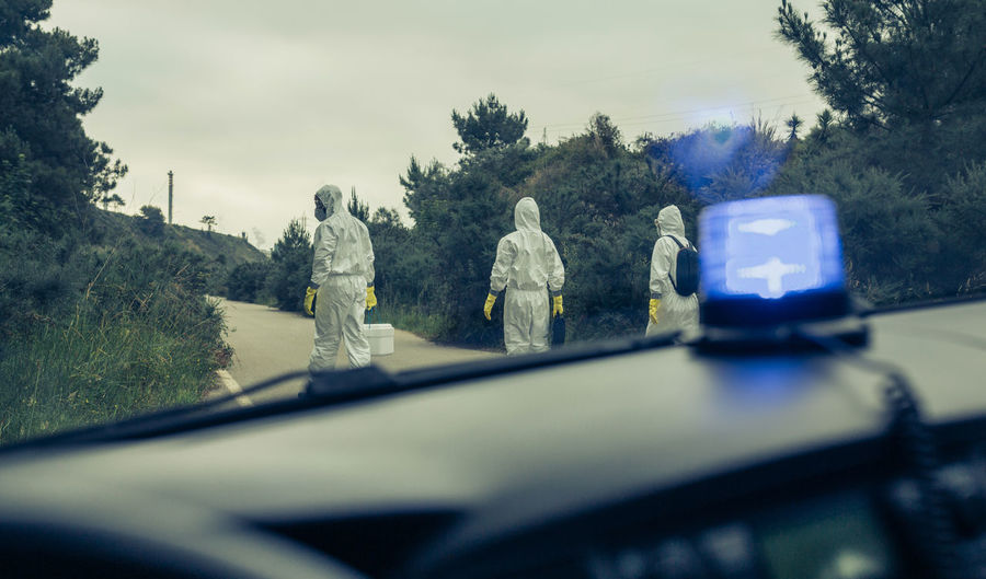 Rear view of people wearing protective suit walking on road seen through car