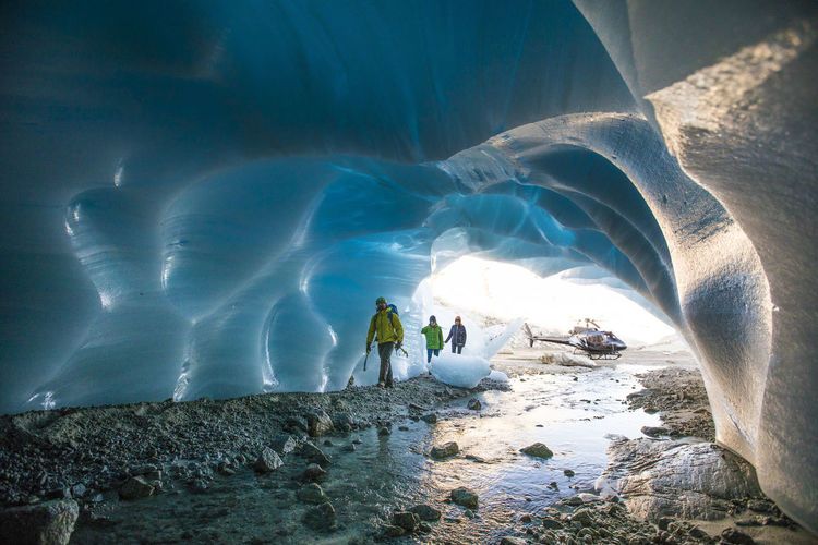 Three ice climbers enter a glacial cave.