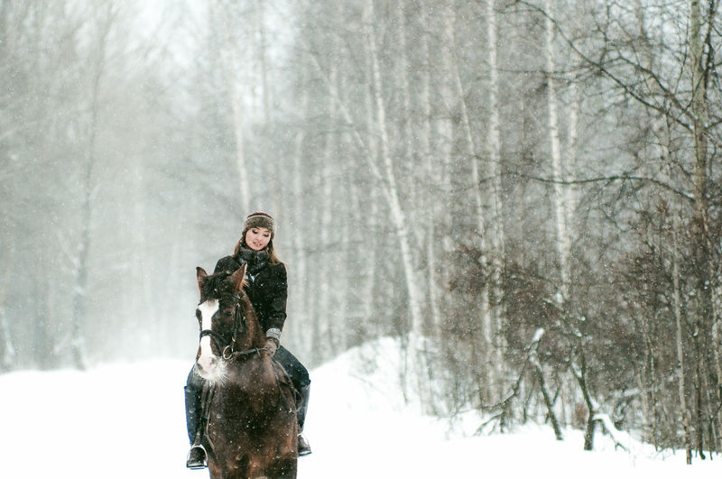 Beautiful woman riding horse on snow covered field