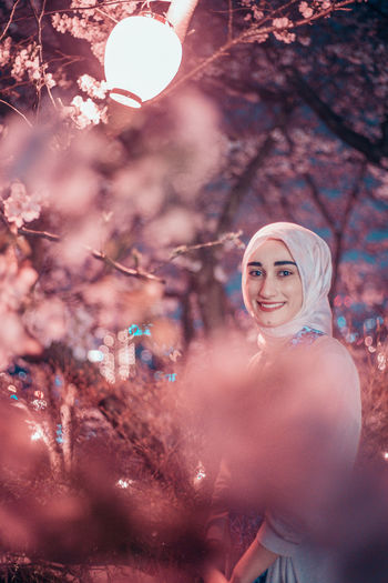 Portrait of a smiling young woman standing by cherry tree