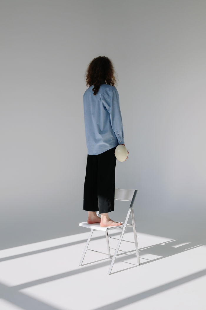 Rear view of woman standing on chair against wall