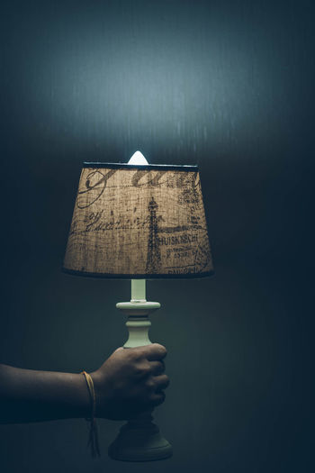 Cropped hand of man holding illuminated lamp against wall at home