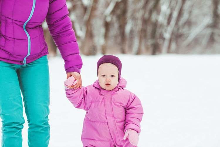 Portrait of cute girl with mother walking on snow during winter
