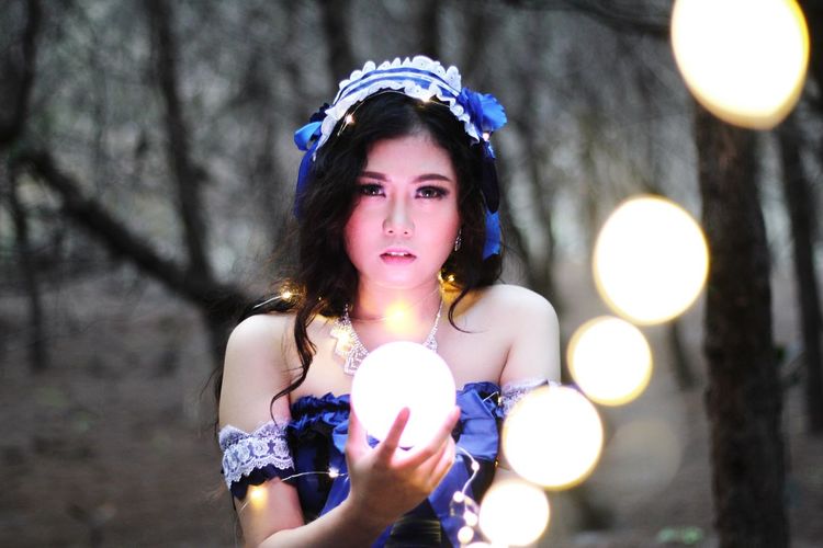 Portrait of a young woman standing against illuminated tree
