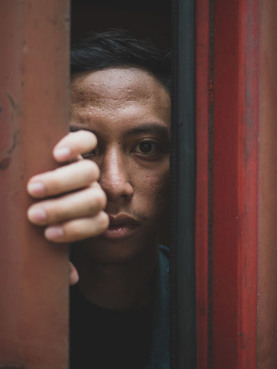 Close-up portrait of young man peeking through door
