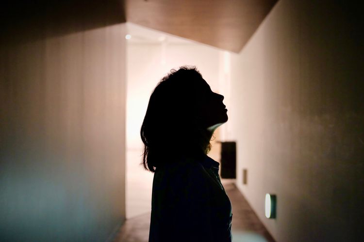 Side view of silhouette woman standing against wall at home