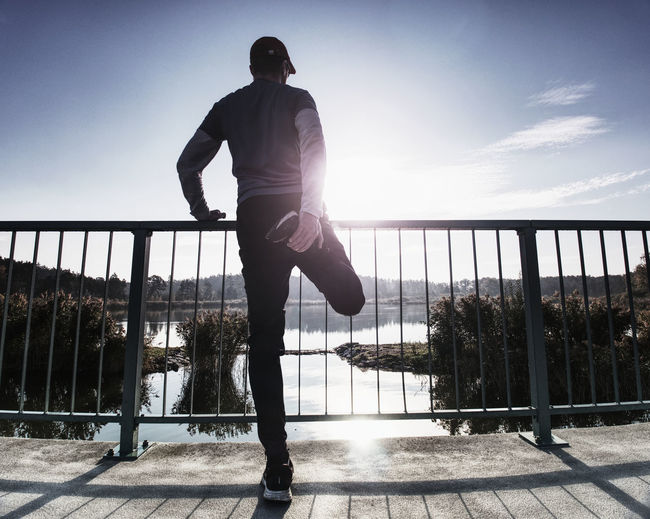 Low section of man standing on railing against sky