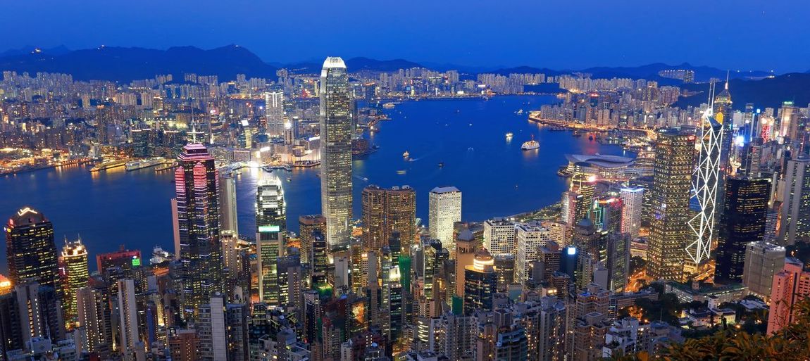 Panoramic view of illuminated cityscape by river against sky