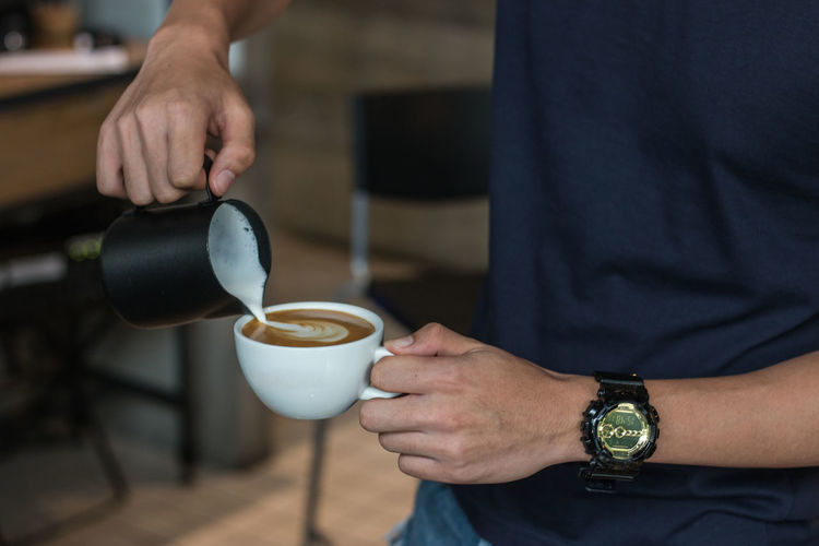 Midsection of barista pouring milk in coffee cup at cafe